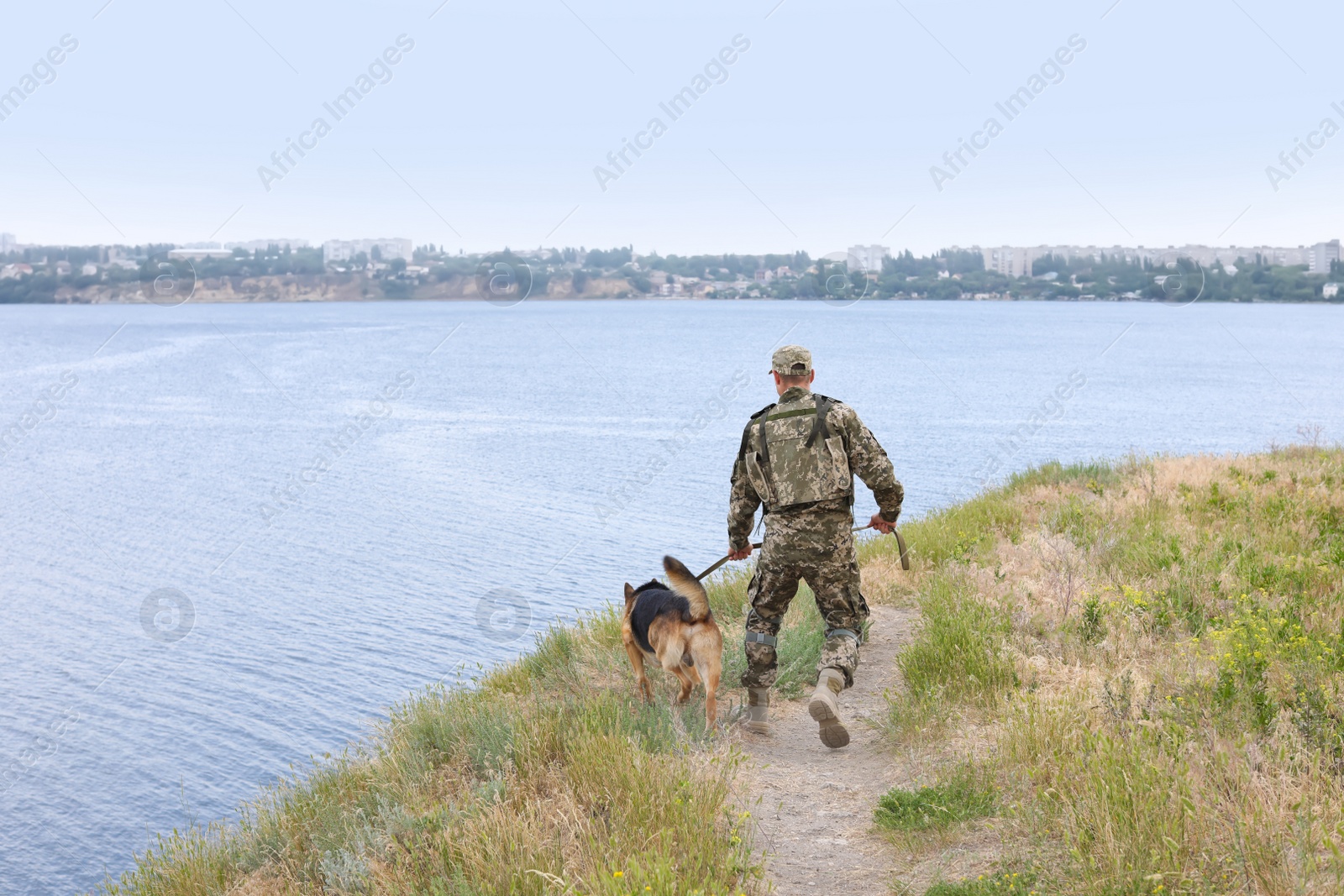 Photo of Man in military uniform with German shepherd dog near river