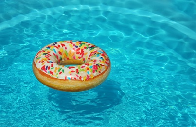 Photo of Bright inflatable doughnut ring floating in swimming pool on sunny day. Space for text