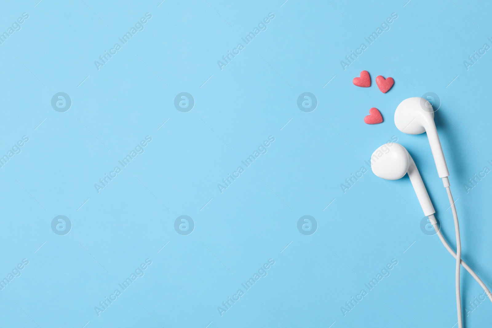Photo of Modern earphones and pink heart shaped sprinkles on light blue background, flat lay with space for text. Listening love music songs