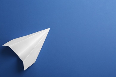 Photo of White paper plane on blue background, top view. Space for text