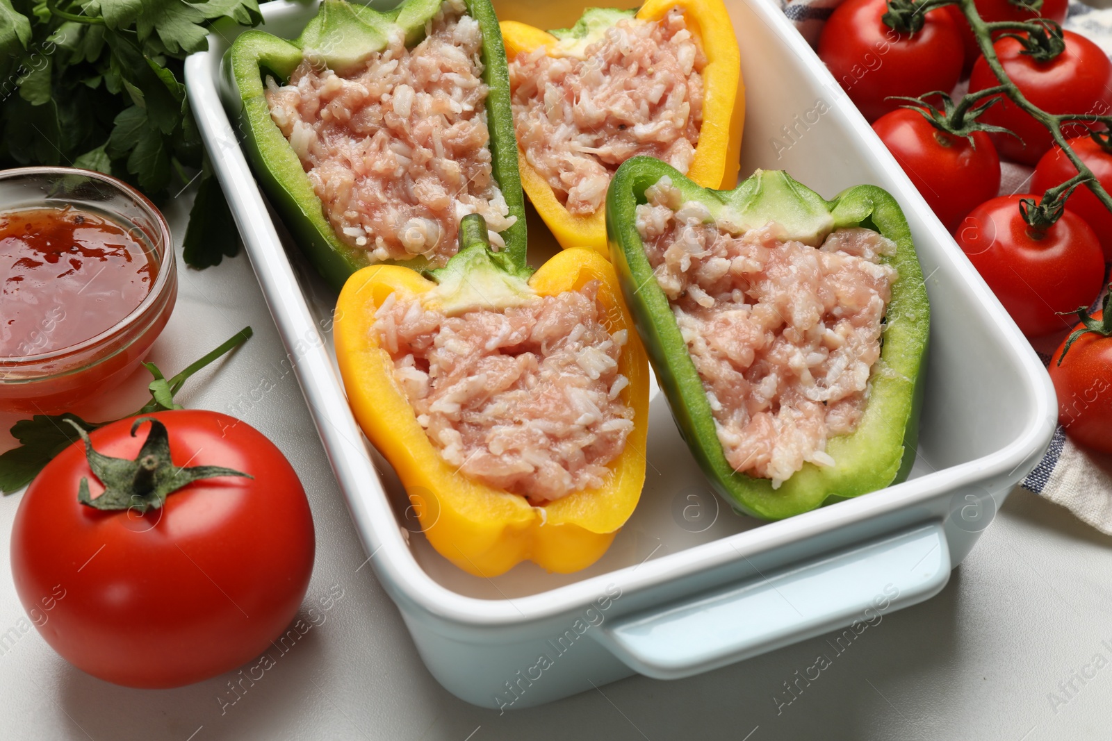 Photo of Raw stuffed peppers and ingredients on white table, closeup
