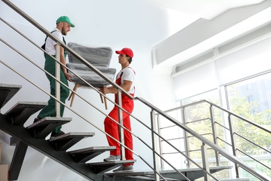 Male movers carrying armchair in new house