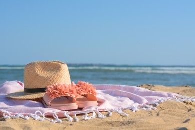 Photo of Blanket with stylish slippers and straw hat on sandy beach near sea. Space for text