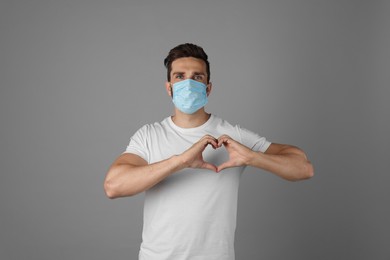 Photo of Man in protective mask making heart with hands on grey background