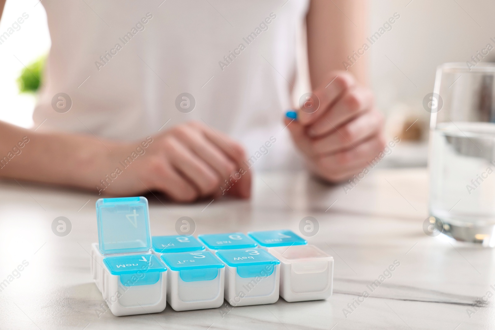 Photo of Woman with pills, organizer and glass of water at white marble table, selective focus