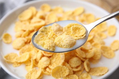 Photo of Breakfast cereal. Eating corn flakes and milk with spoon from bowl on table, closeup