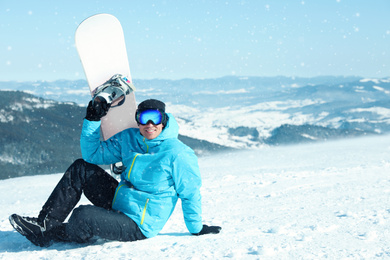 Photo of Happy man with snowboard in mountains. Winter vacation