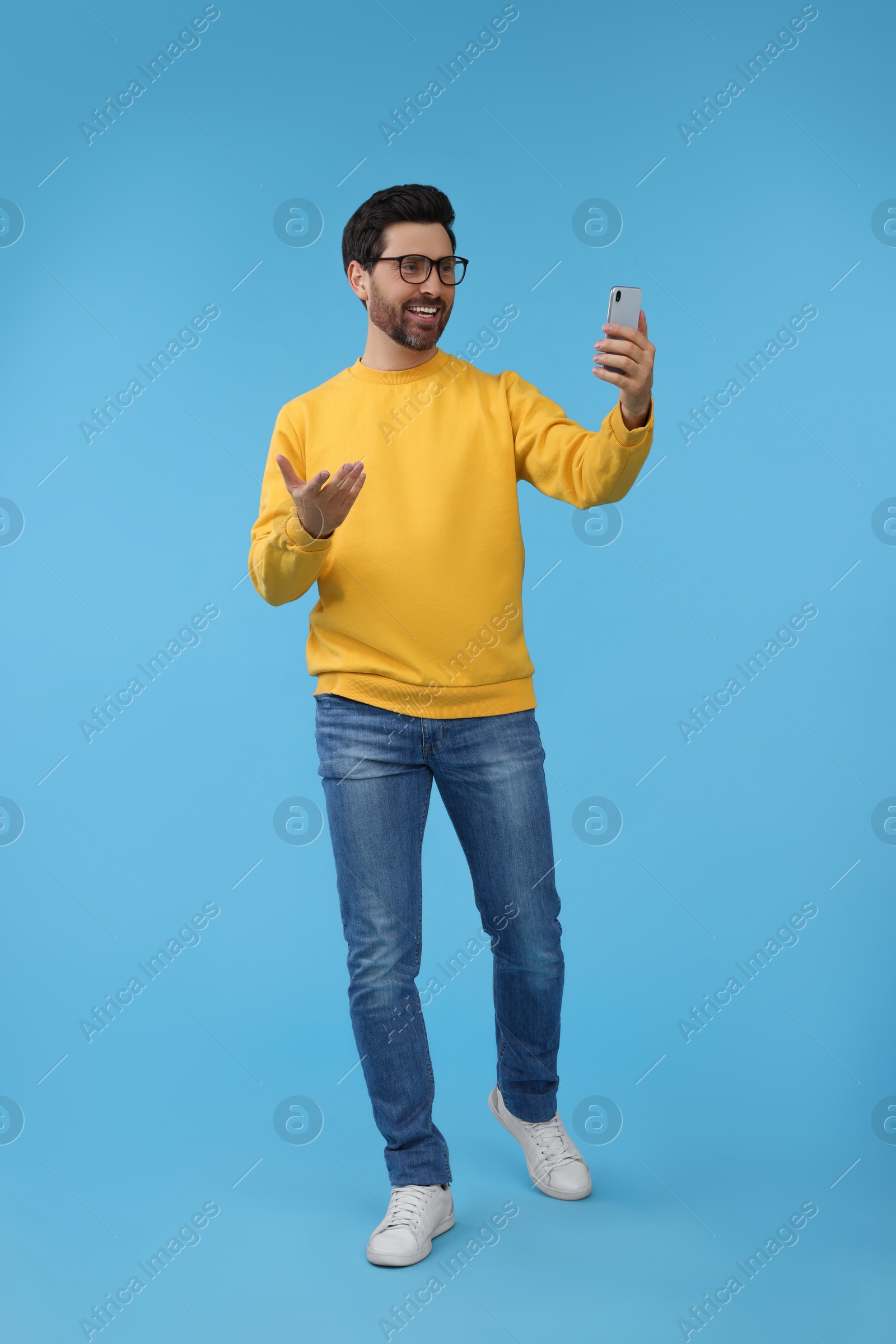 Photo of Smiling man taking selfie with smartphone on light blue background