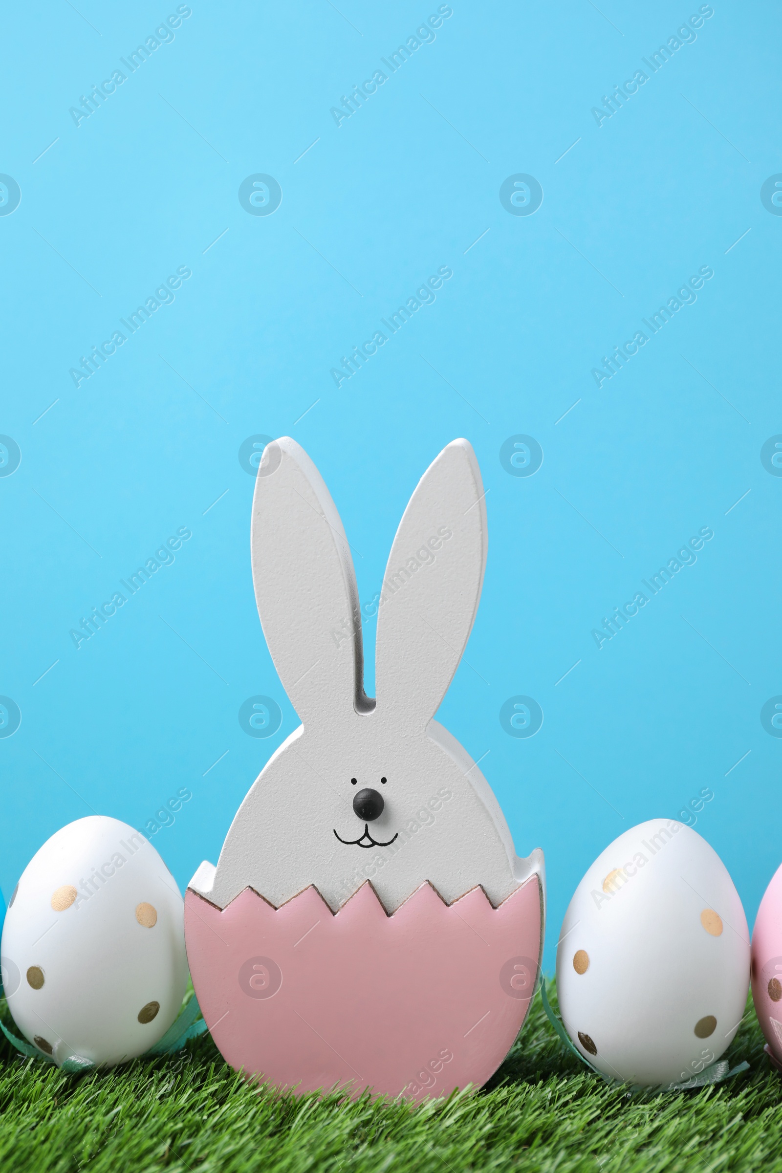 Photo of Easter bunny figure and dyed eggs on green grass against light blue background