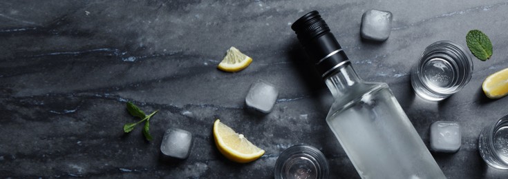 Bottle of vodka, shot glasses, lemon, mint and ice on black marble table, flat lay. Space for text. Banner design