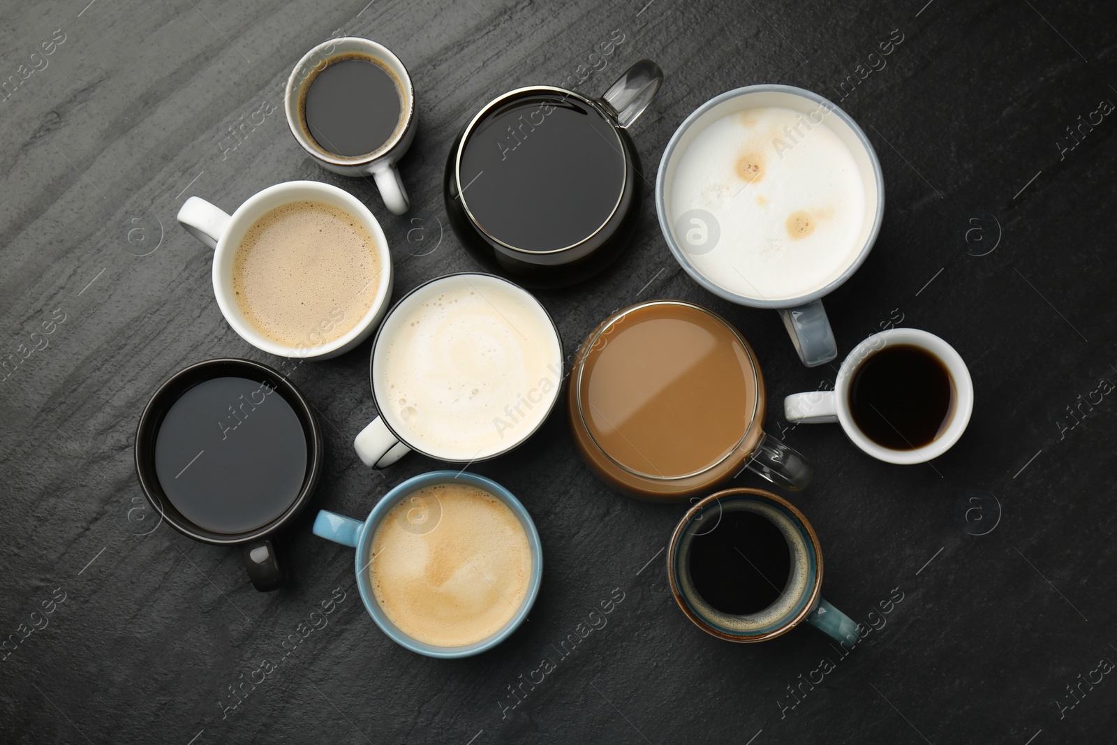 Photo of Different coffee drinks in cups on dark textured table, flat lay