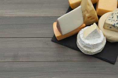 Different types of delicious cheeses on wooden table. Space for text