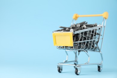 Photo of Metal nails in shopping cart on light blue background, closeup. Space for text