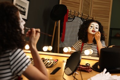 Young woman applying mime makeup near mirror indoors