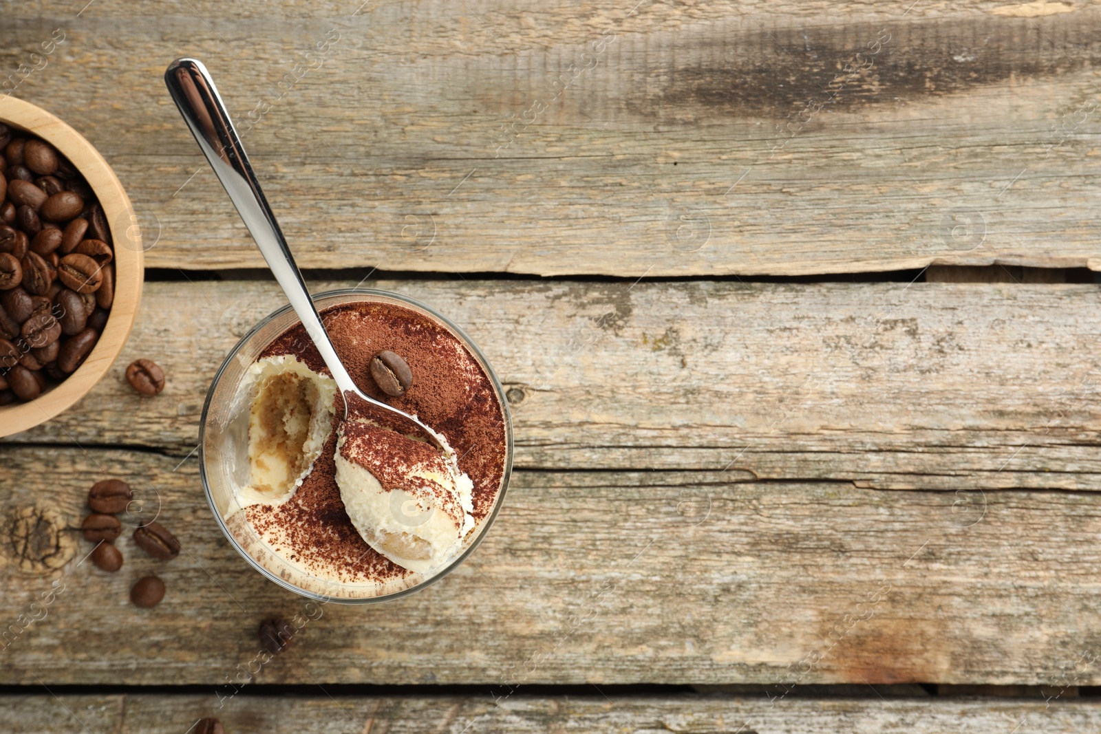 Photo of Delicious tiramisu in glass, spoon and coffee beans on wooden table, top view. Space for text