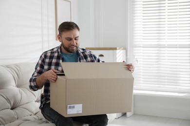 Photo of Happy young man opening parcel at home