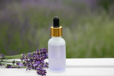 Photo of Bottle of essential oil and lavender flowers on white wooden table in field