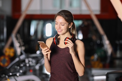 Photo of Young woman with headphones and mobile device at gym