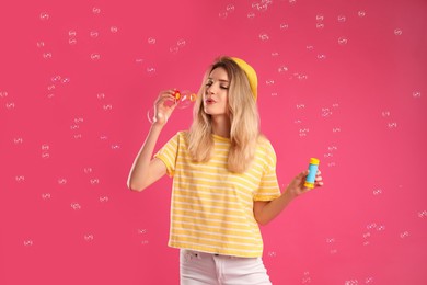 Young woman blowing soap bubbles on pink background