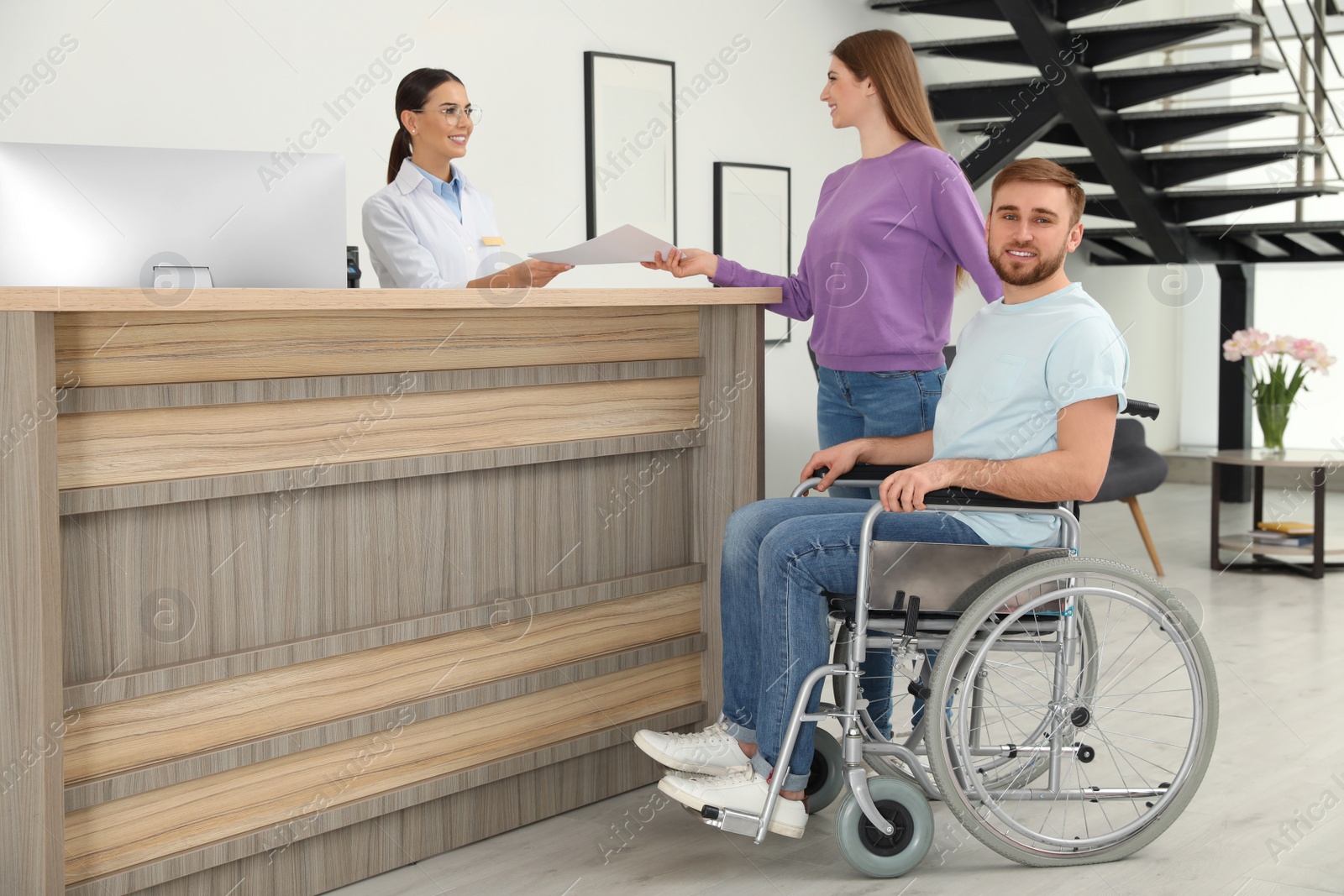 Photo of Professional receptionist working with woman and handicapped man at desk in clinic
