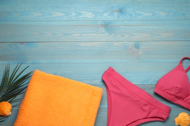 Photo of Beach towel and swimsuit on light blue wooden background, flat lay. Space for text