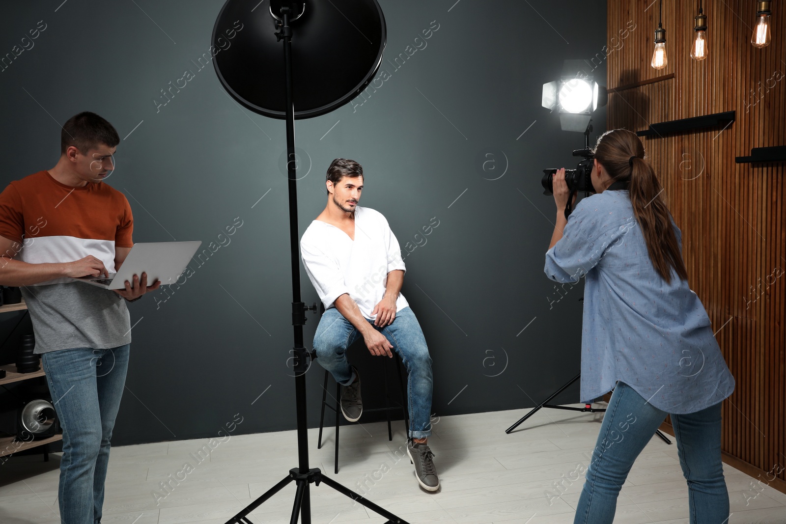 Photo of Professional photographer with assistant taking picture of young man in modern studio