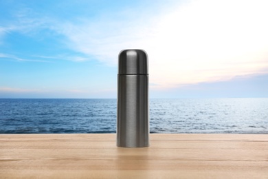 Image of Thermos on wooden table near sea under blue sky