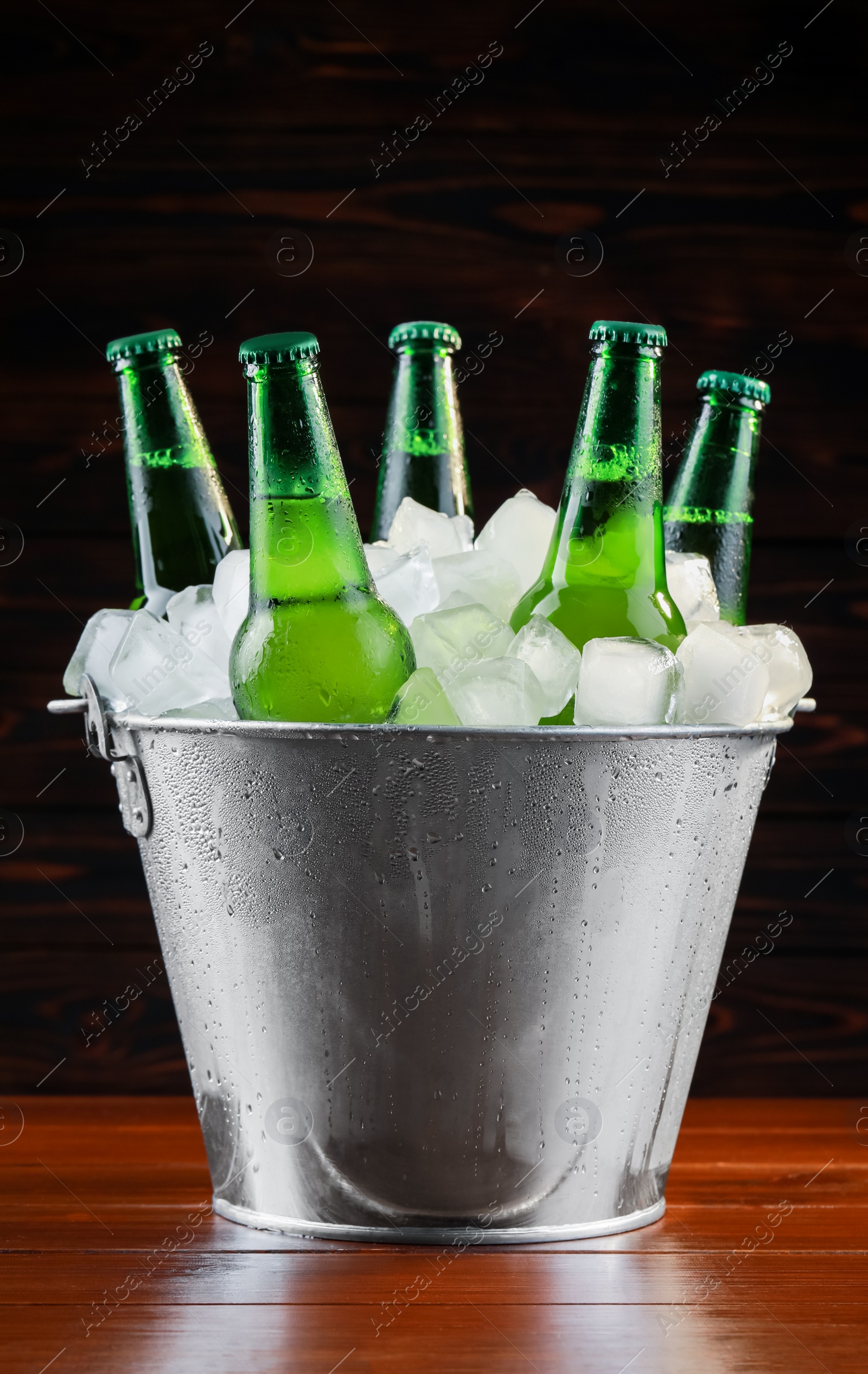 Photo of Metal bucket with bottles of beer and ice cubes on wooden background