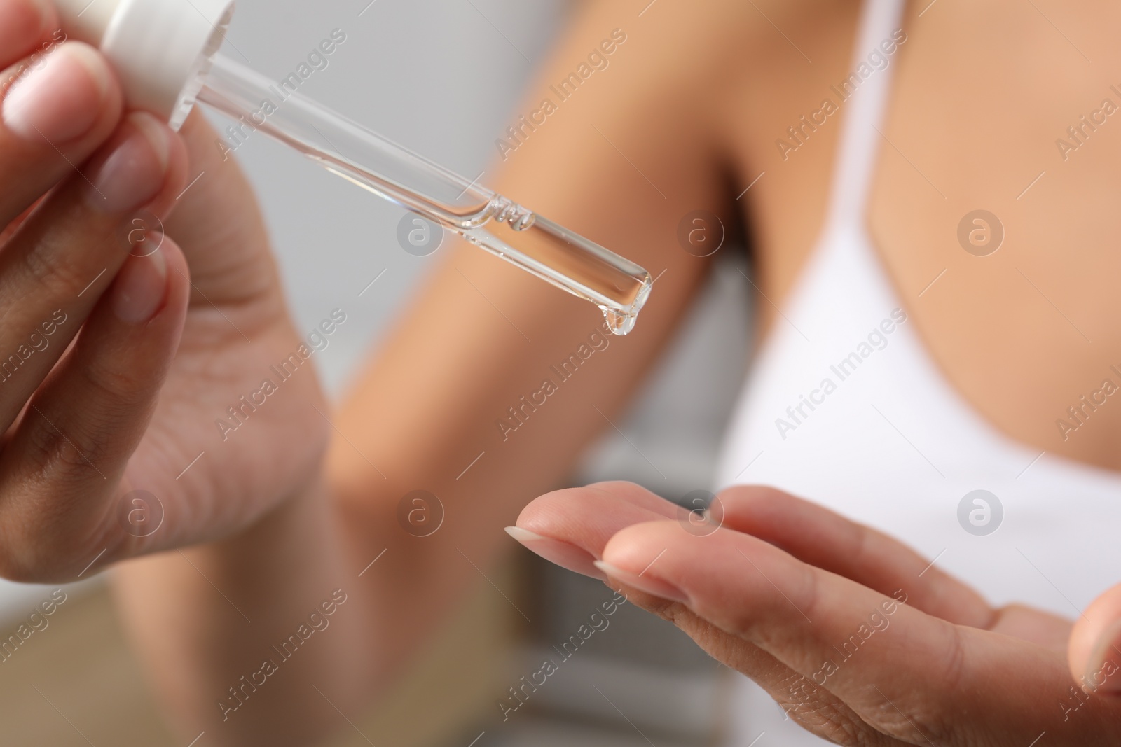 Photo of Woman applying cosmetic serum onto her finger on blurred background, closeup