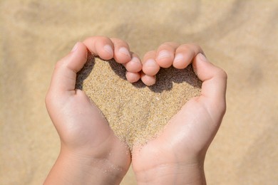 Photo of Child holding sand in hands outdoors, closeup. Fleeting time concept