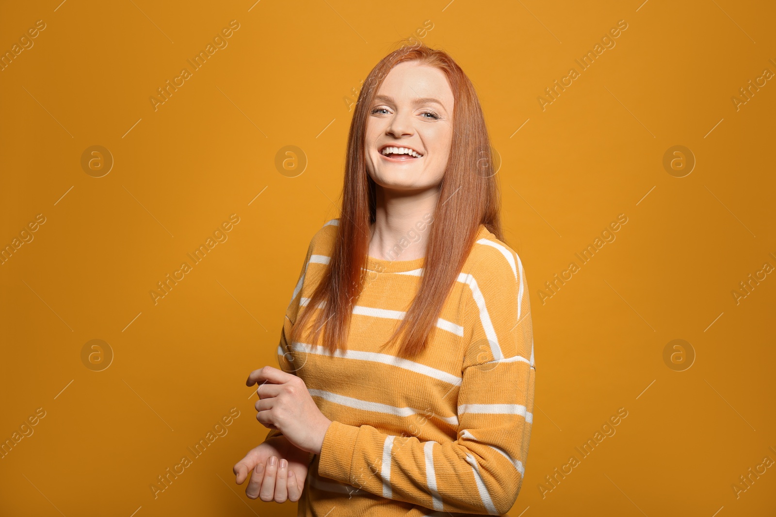 Photo of Candid portrait of happy young woman with charming smile and gorgeous red hair on yellow background