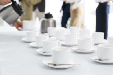 Photo of Waitress pouring hot drink during coffee break, focus on table with cups