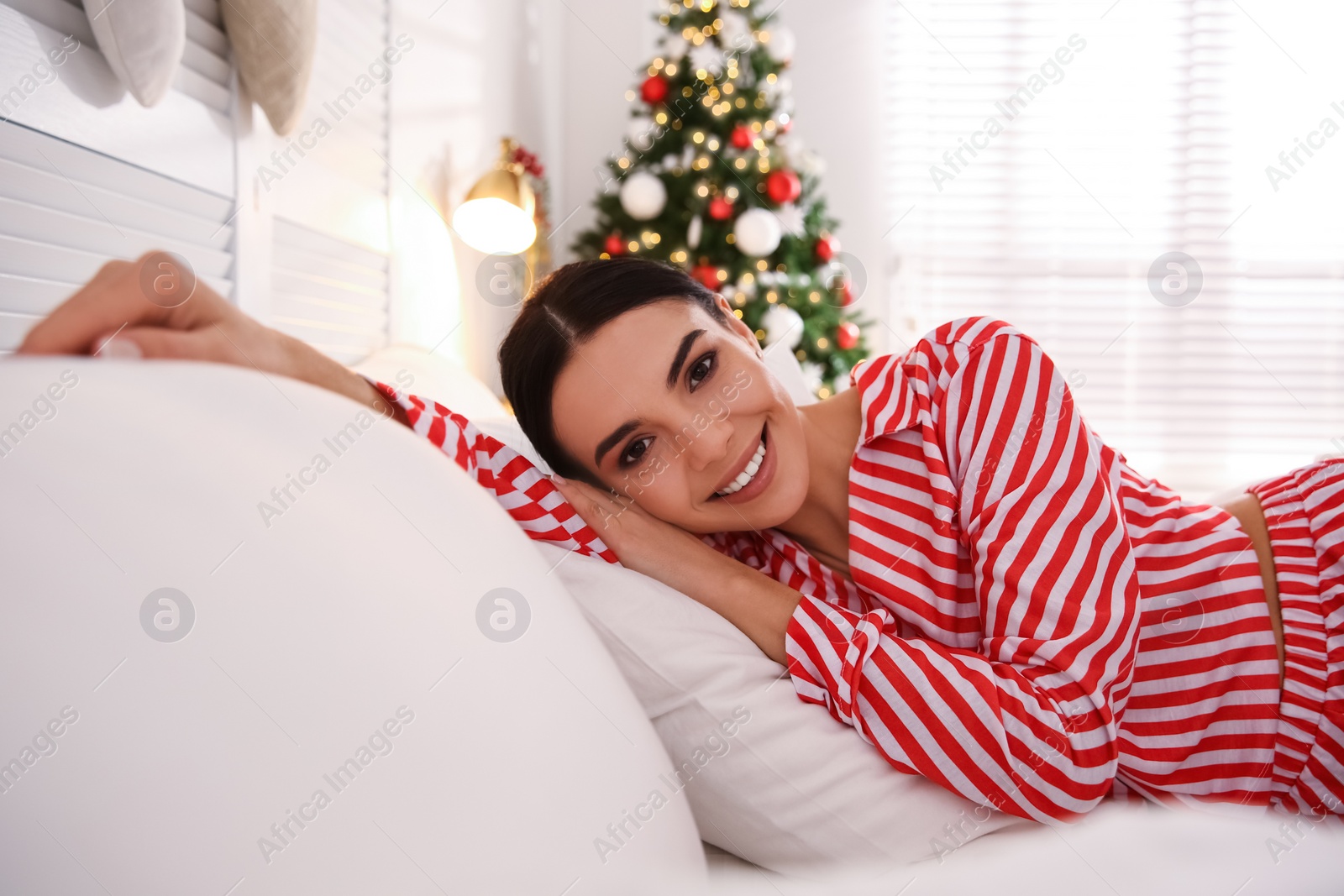 Photo of Young woman lying on bed in room with Christmas tree