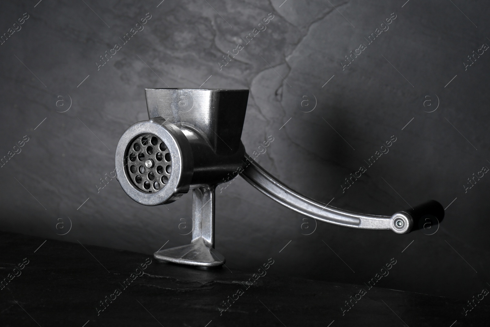Photo of Metal manual meat grinder on dark table against black background
