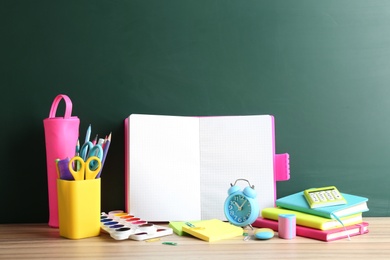 Photo of Different school stationery and blank notebook on table near chalkboard. Space for text