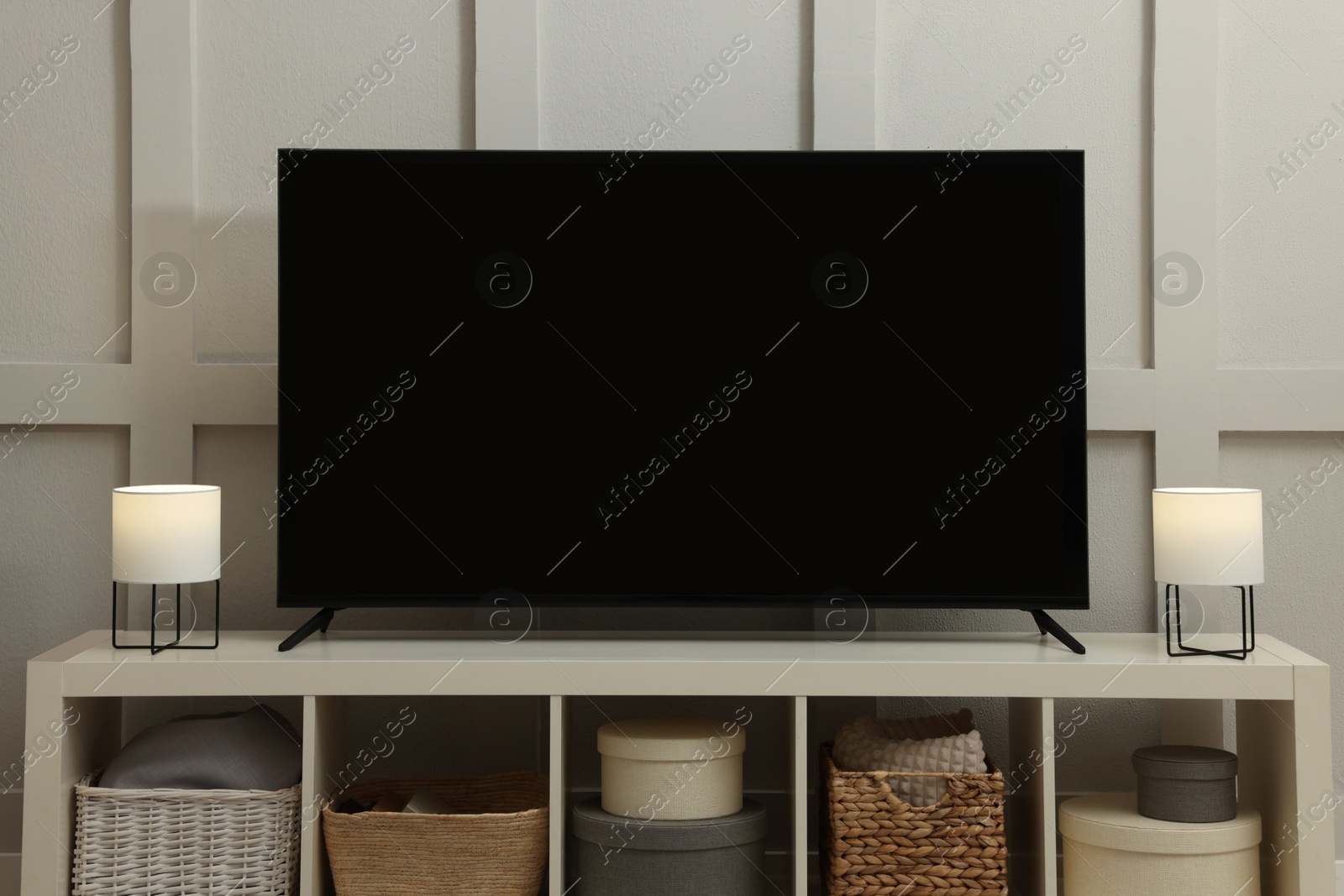 Photo of Modern TV and lamps on cabinet near white wall indoors. Interior design