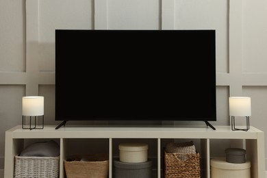 Photo of Modern TV and lamps on cabinet near white wall indoors. Interior design