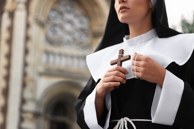 Photo of Young nun with Christian cross near cathedral outdoors, closeup. Space for text