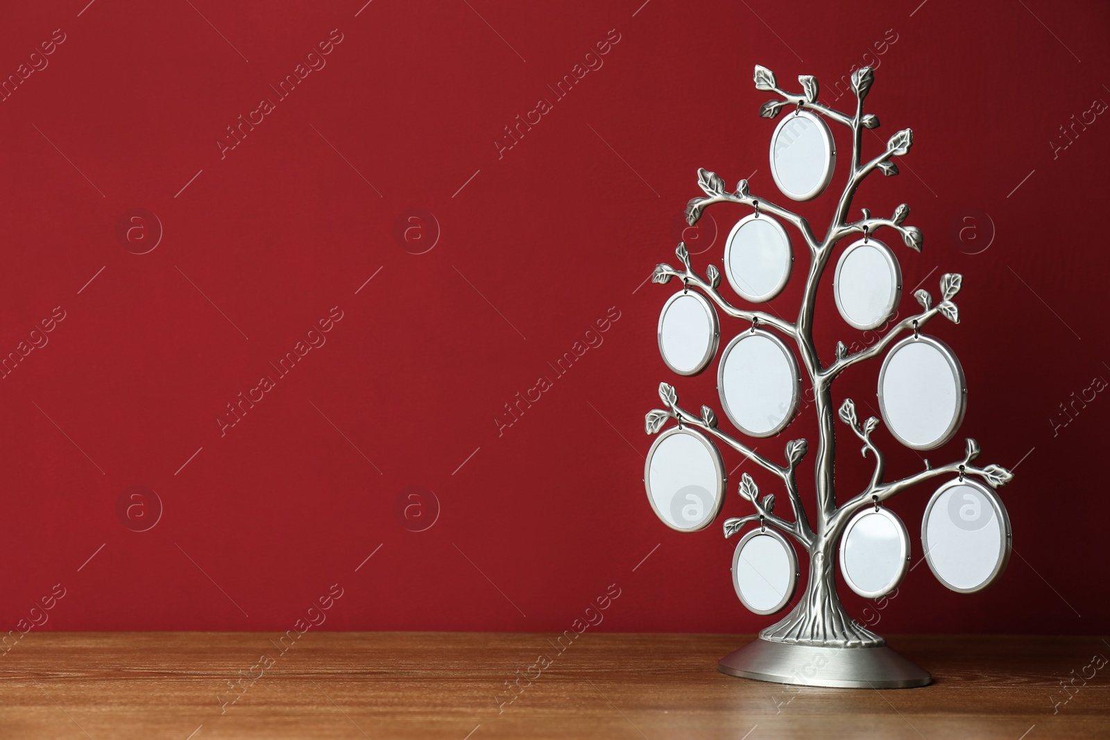 Photo of Blank metal family tree frame on wooden table against red background. Space for text