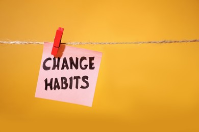 Photo of Paper notes with phrase Change Habits hanging on rope against orange background