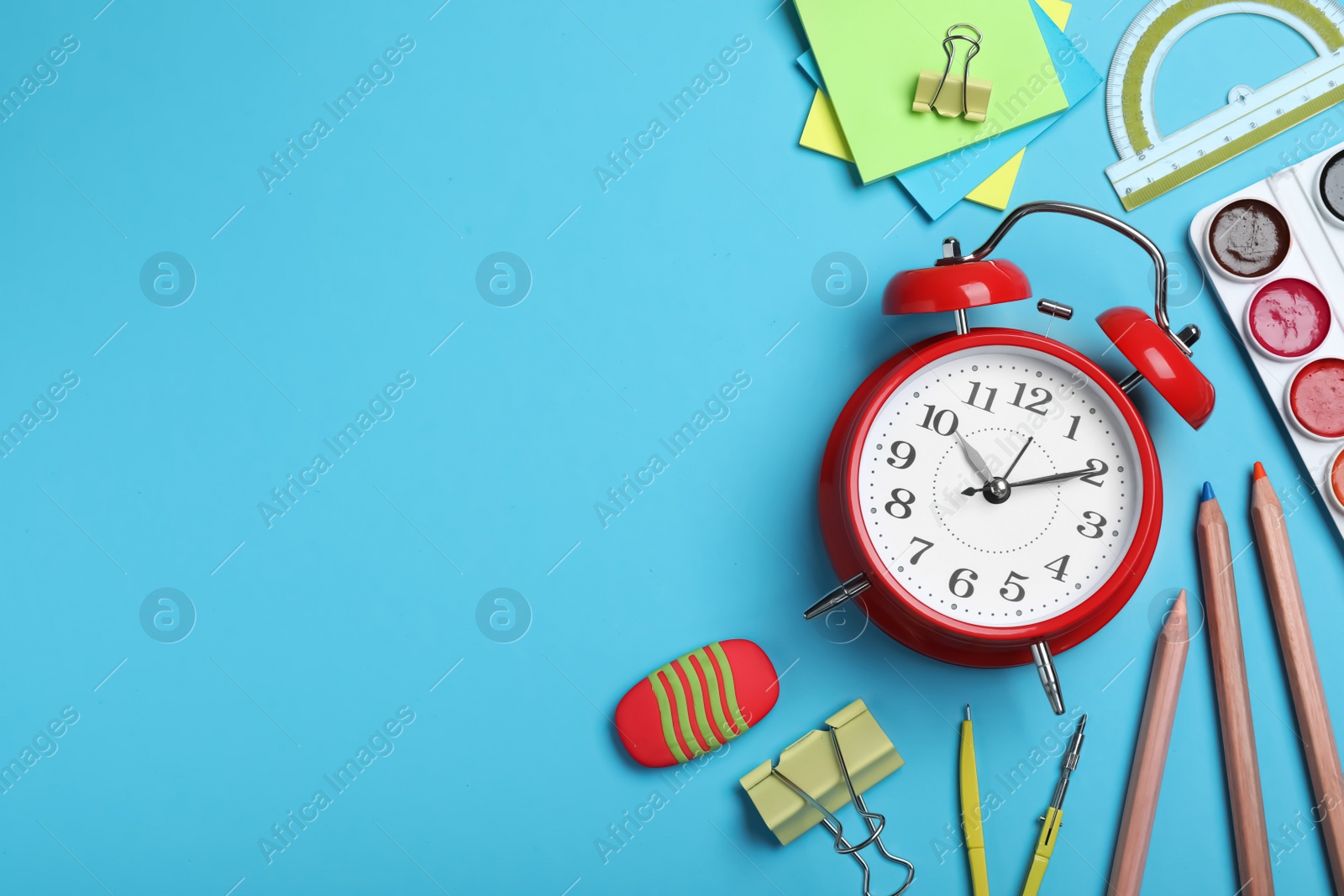 Photo of Flat lay composition with alarm clock and different stationery on light blue background, space for text. School time