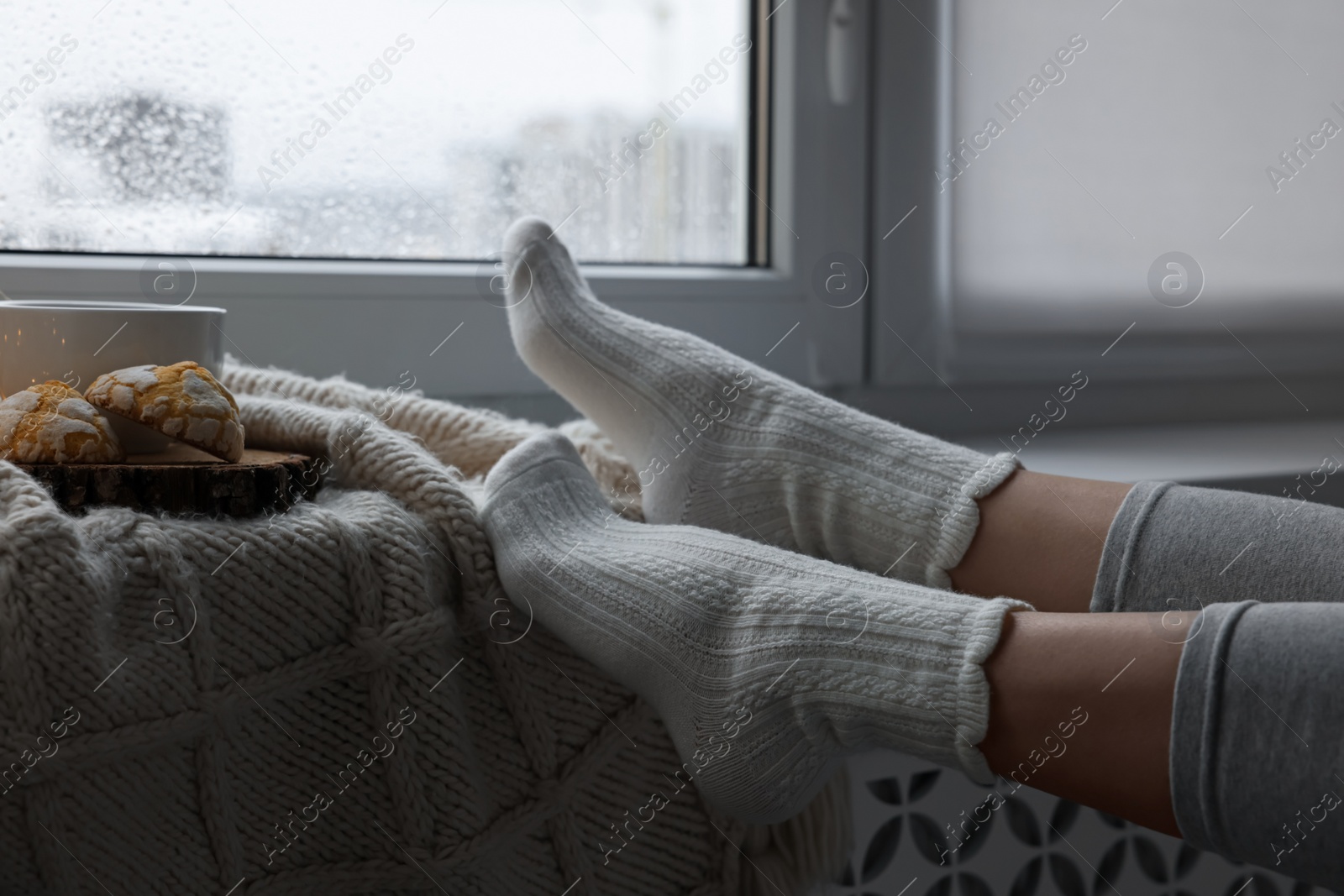 Photo of Woman in knitted socks relaxing near window at home, closeup. Space for text