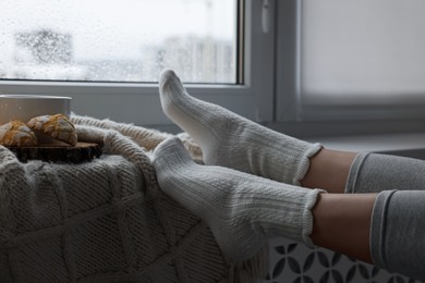 Woman in knitted socks relaxing near window at home, closeup. Space for text