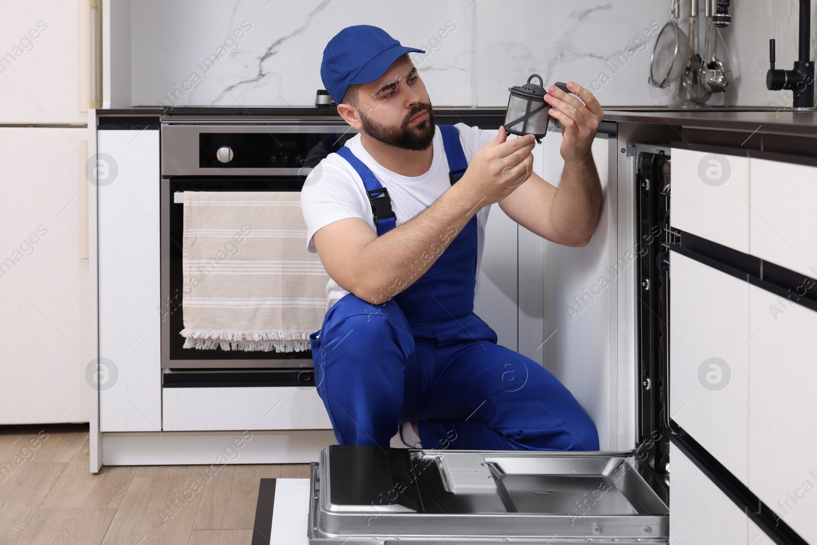 Photo of Repairman holding drain filter near dishwasher in kitchen