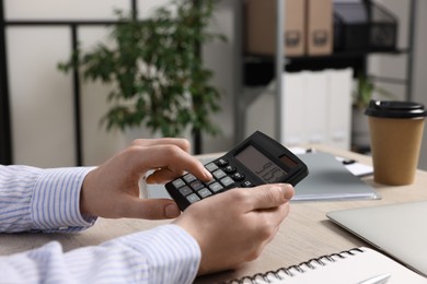 Photo of Man using calculator at wooden table in office, closeup