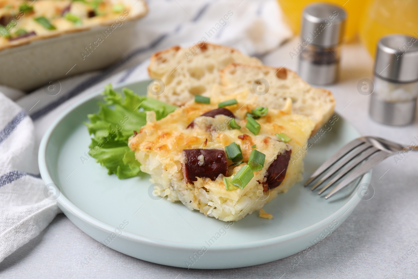 Photo of Tasty sausage casserole with green onion served on light grey table, closeup