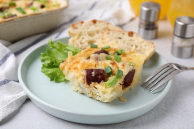 Photo of Tasty sausage casserole with green onion served on light grey table, closeup