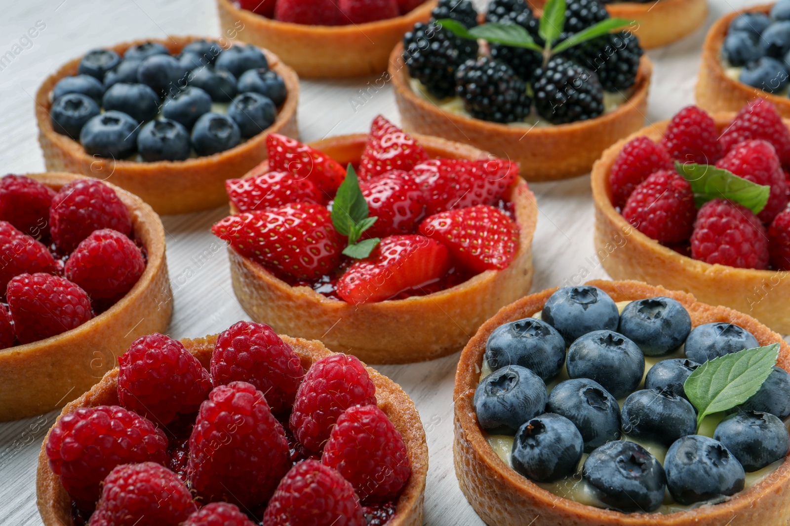 Photo of Tartlets with different fresh berries on white table, closeup. Delicious dessert