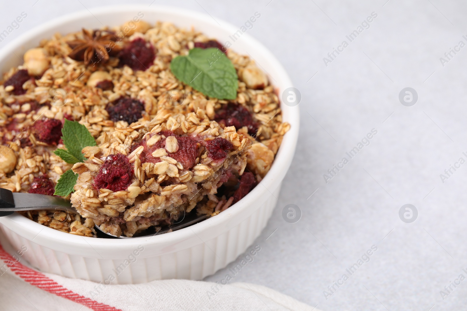Photo of Tasty baked oatmeal with berries and nuts on light table, closeup. Space for text