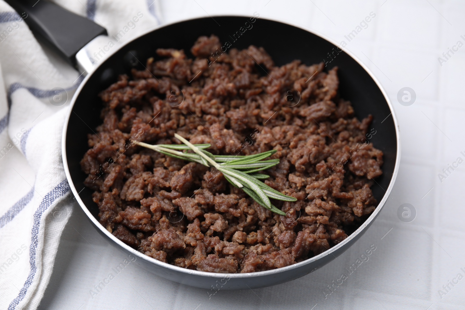 Photo of Fried ground meat in frying pan and rosemary on white tiled table, closeup